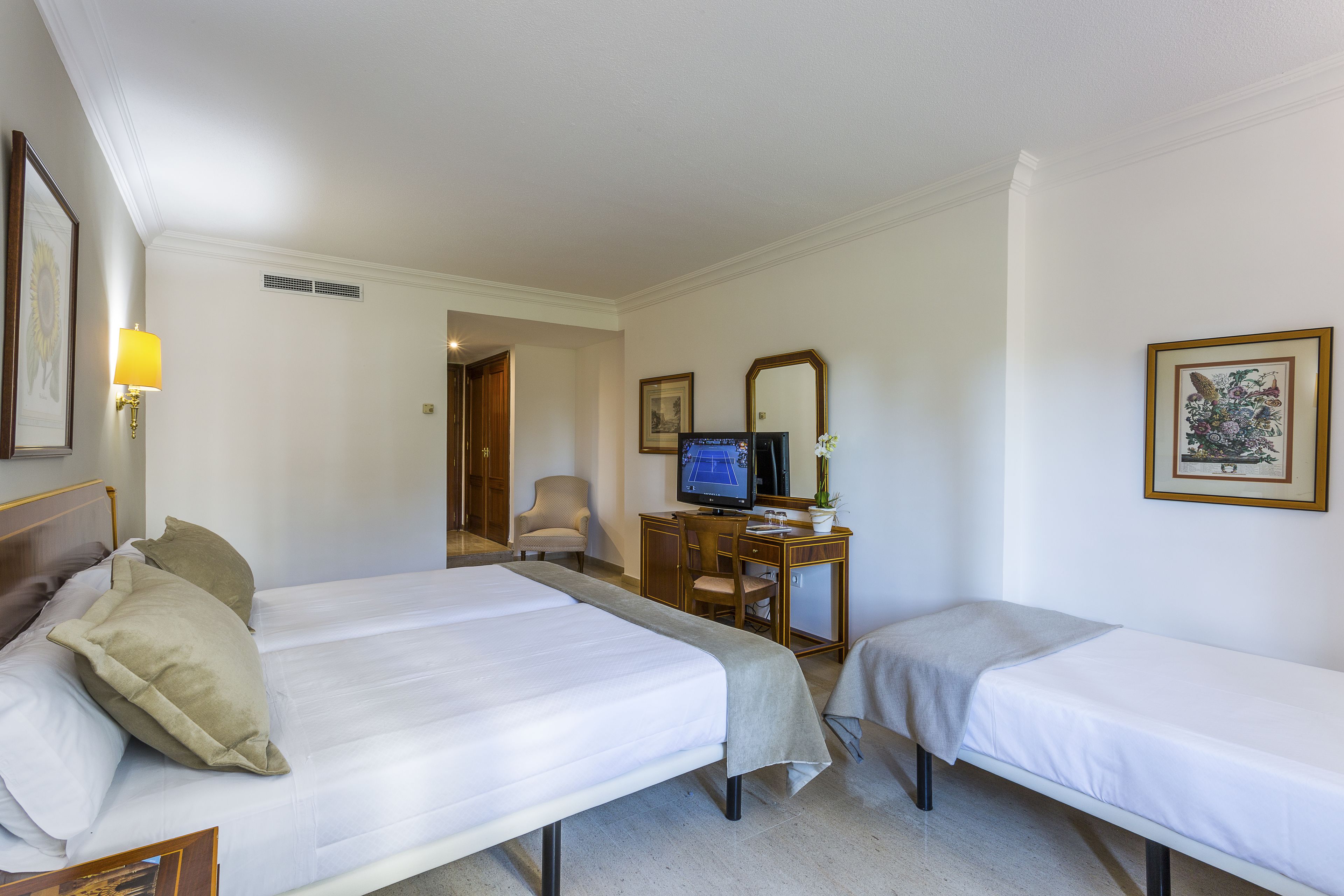 A hotel room with two beds, a desk with a computer, a chair, and a television.