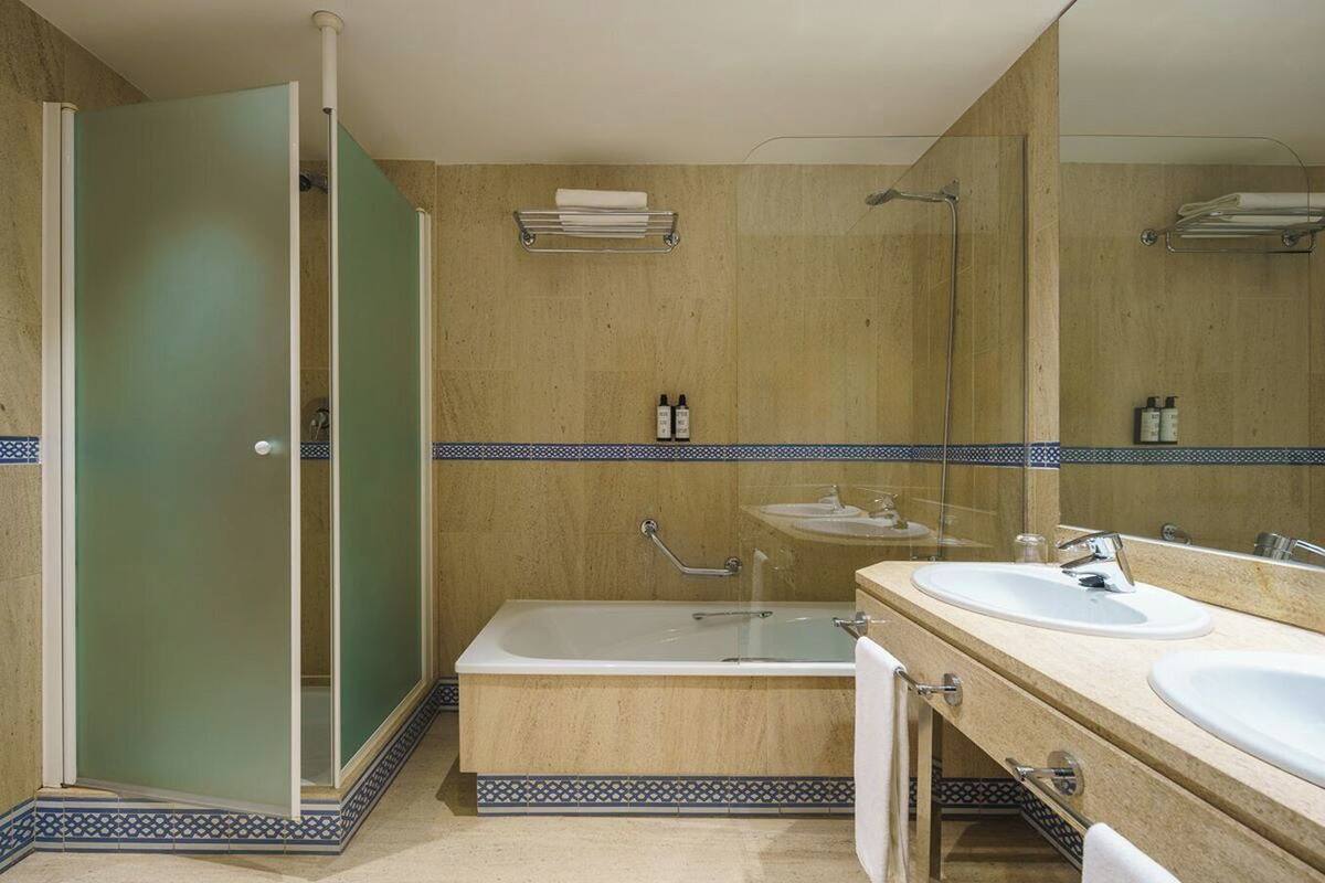 Een badkamer met een glazen douchecabine, een badkuip en twee wastafels met spiegels.