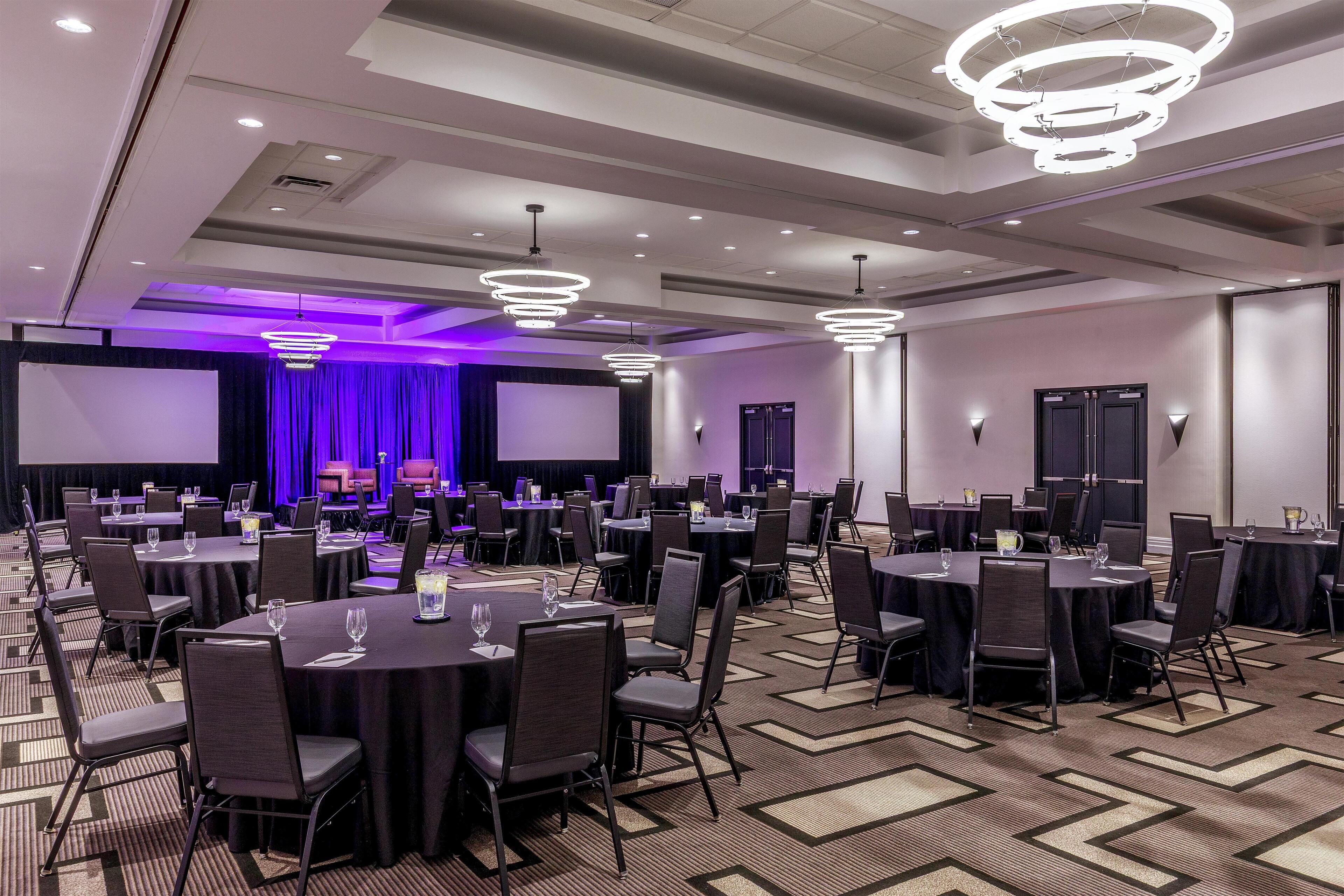 A conference room with round tables, chairs, and a stage with curtains.