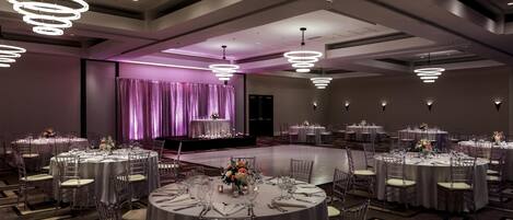 Un salón de banquetes con varias mesas redondas, sillas transparentes e iluminación colgante moderna.
