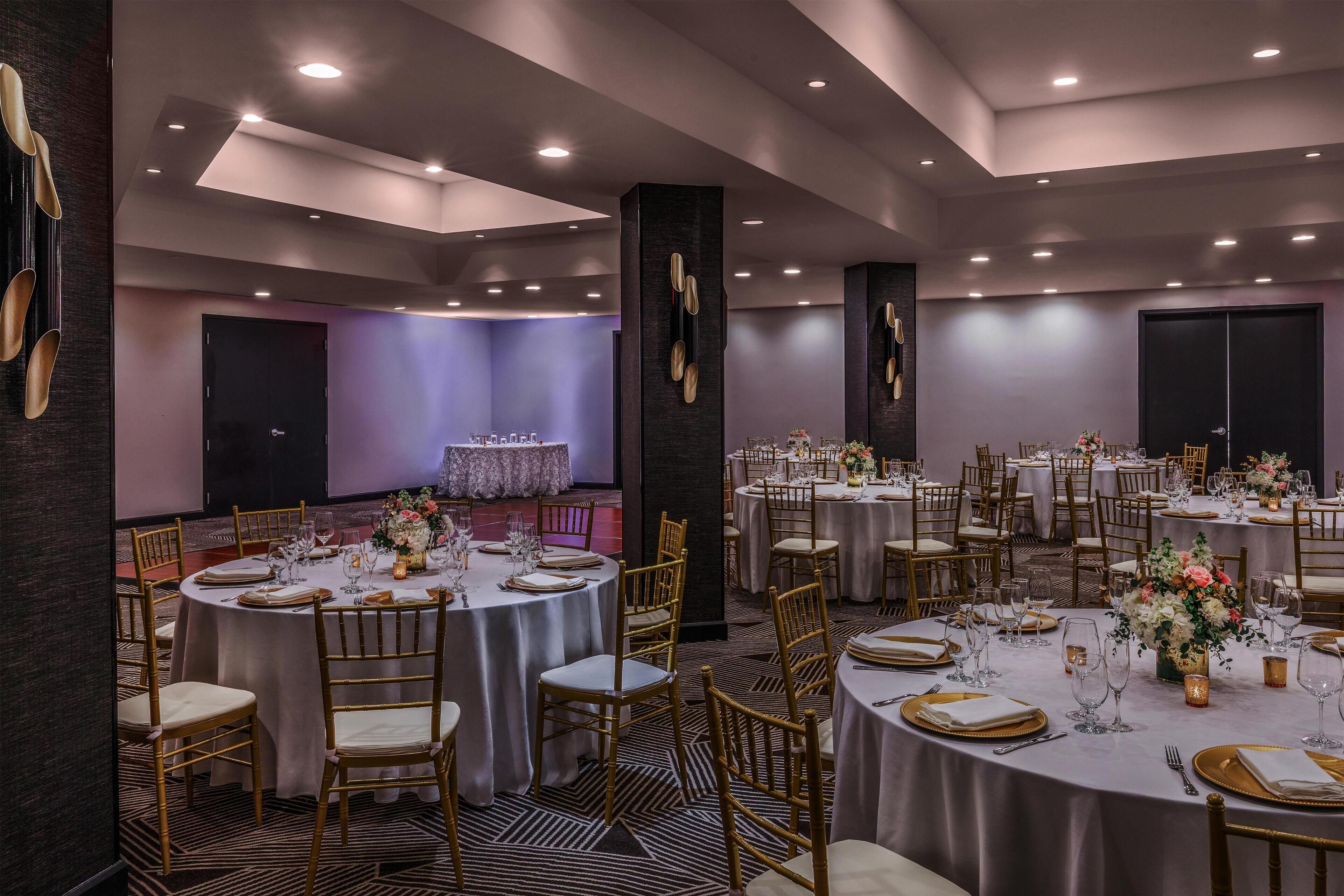 Uma sala de banquetes com mesas redondas, cadeiras e arranjos florais.