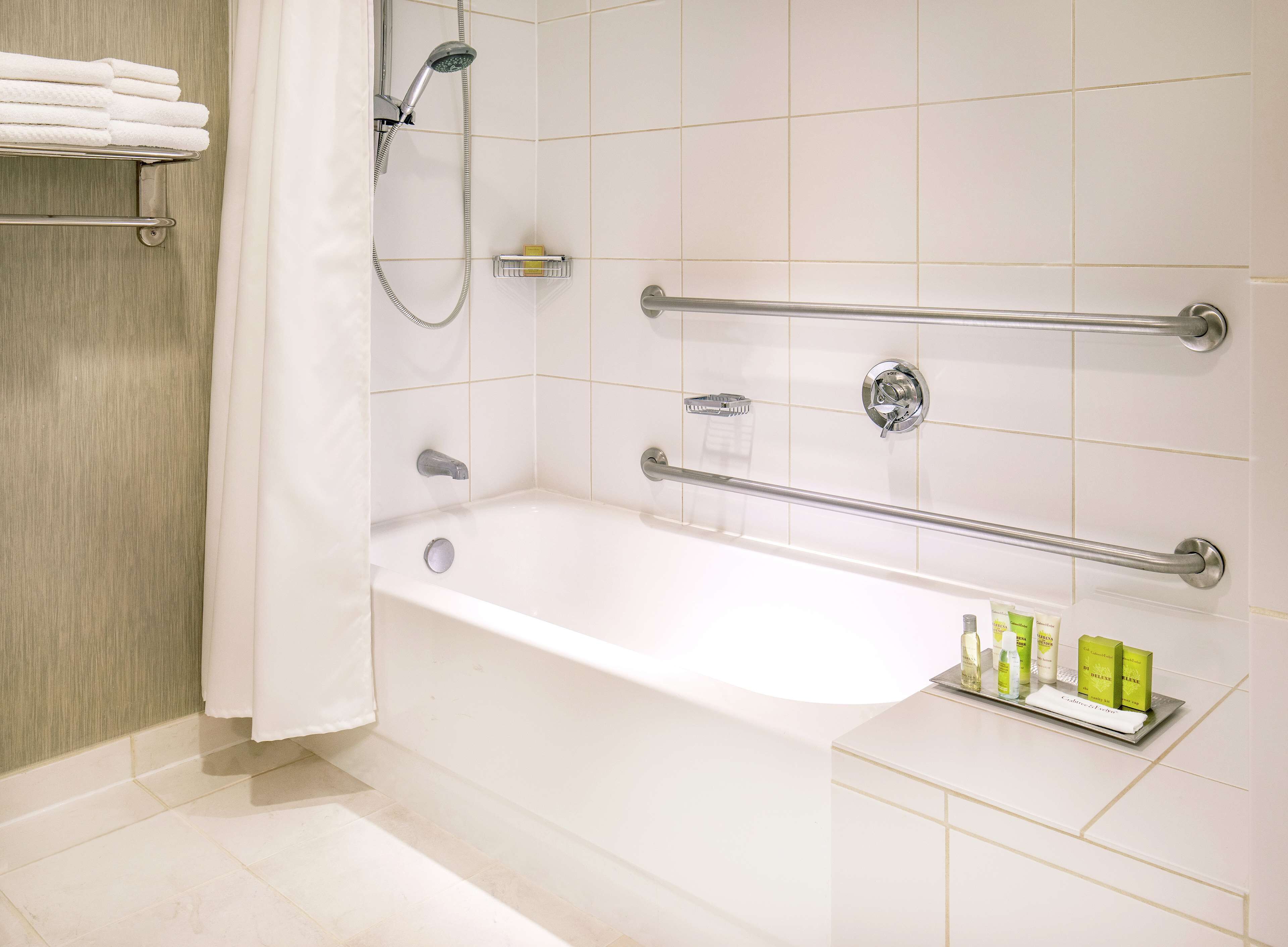 A modern bathroom with a bathtub, grab bars, a showerhead, and a shelf with toiletries.