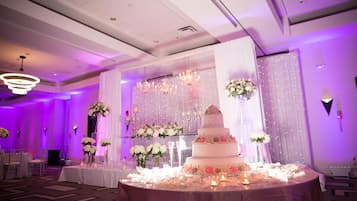 Salón de recepción de bodas con un pastel de varios niveles, centros de mesa florales e iluminación ambiental.