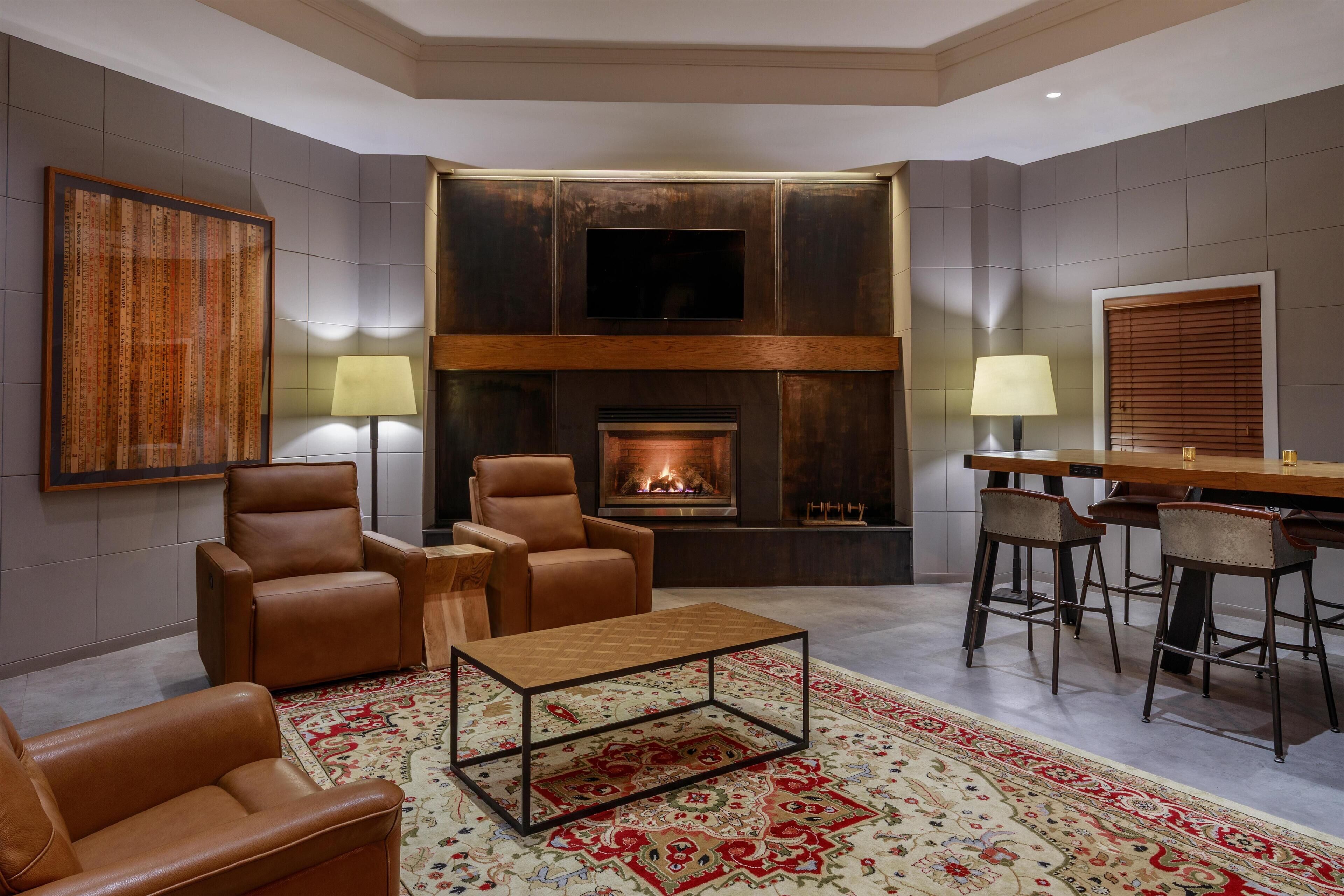 A modern living room with leather chairs, a coffee table, a fireplace, and a bar area.
