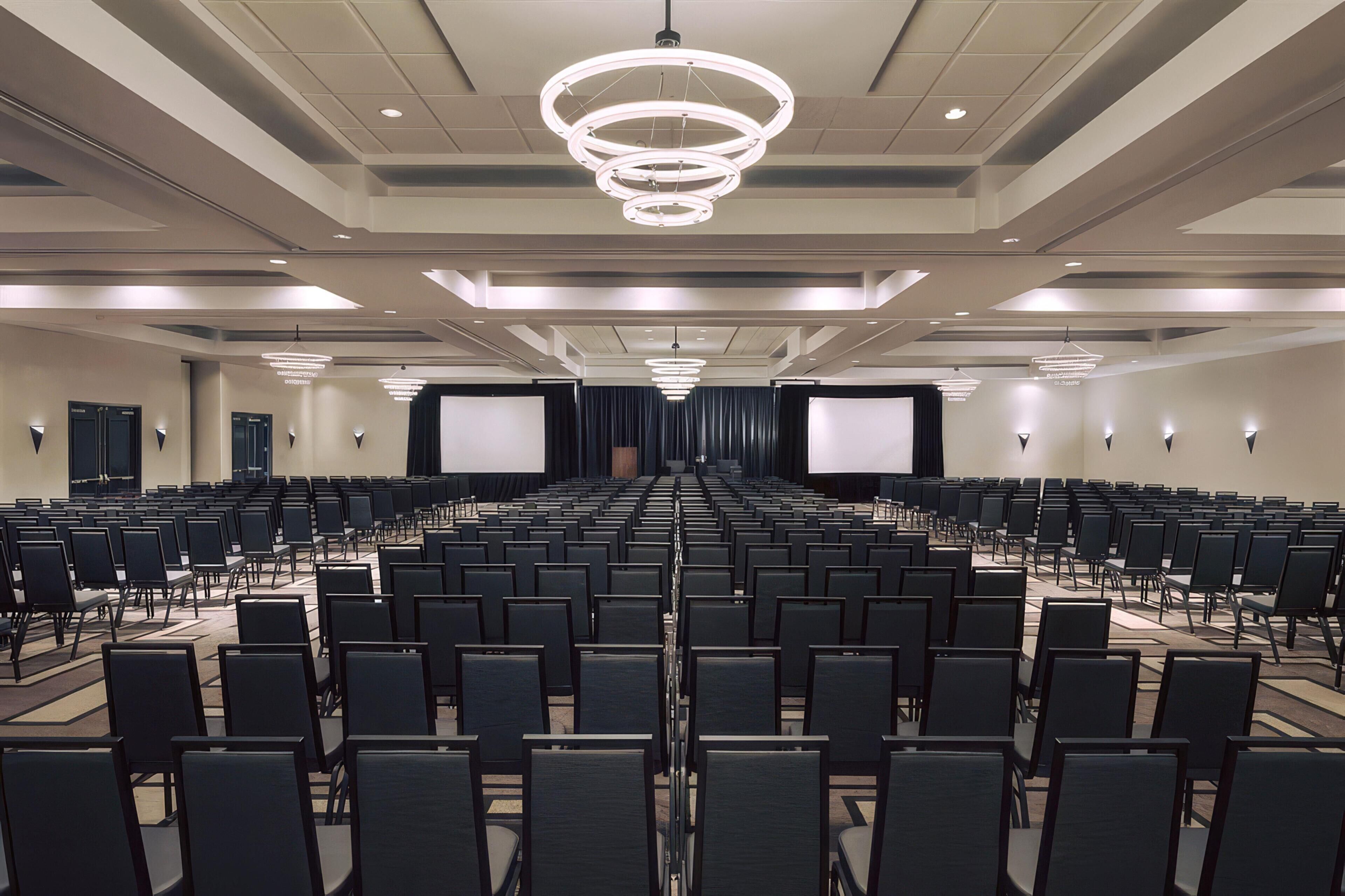 A conference room with rows of chairs, a large screen, and a modern chandelier.