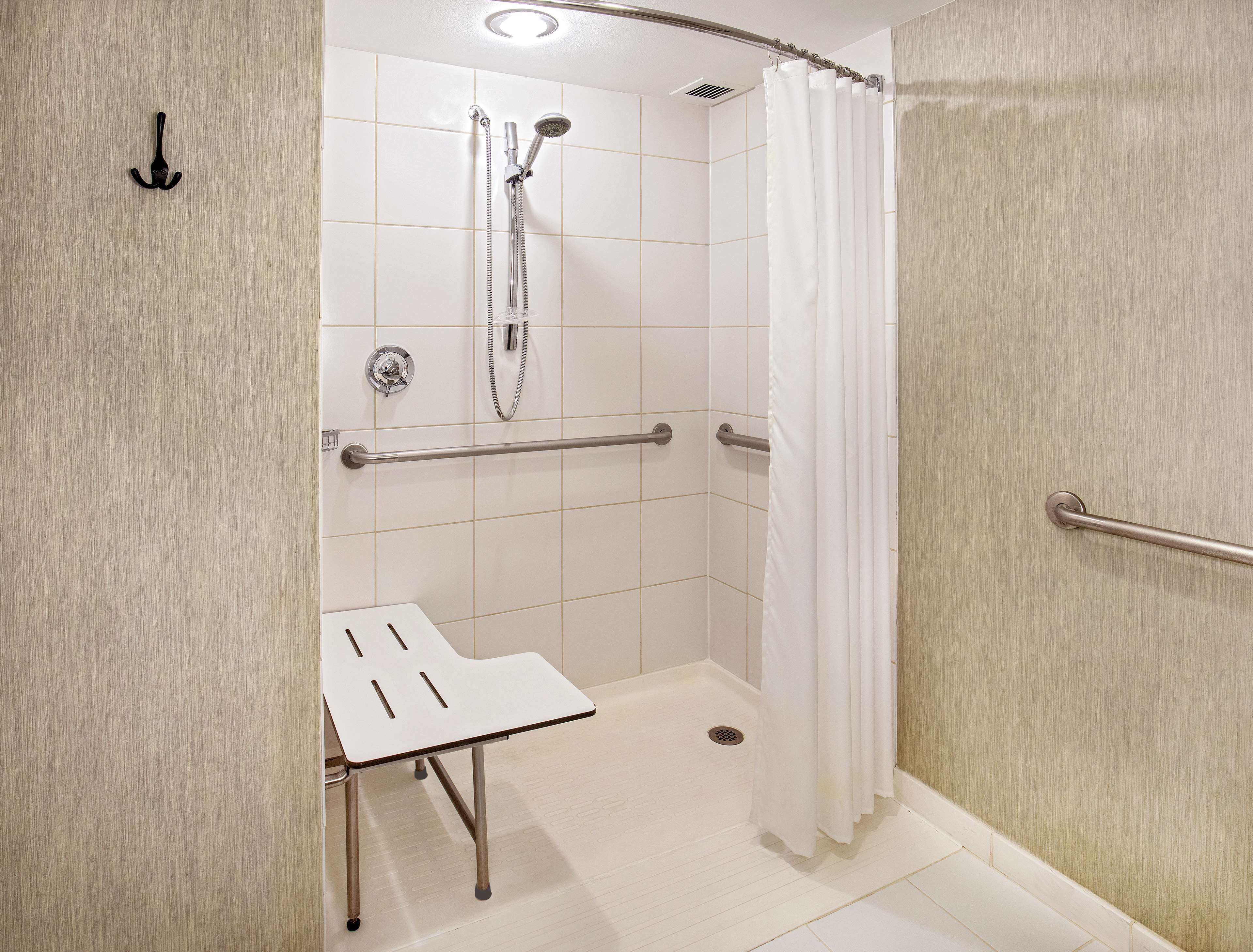 A modern bathroom with a shower, grab bars, and a white sink.