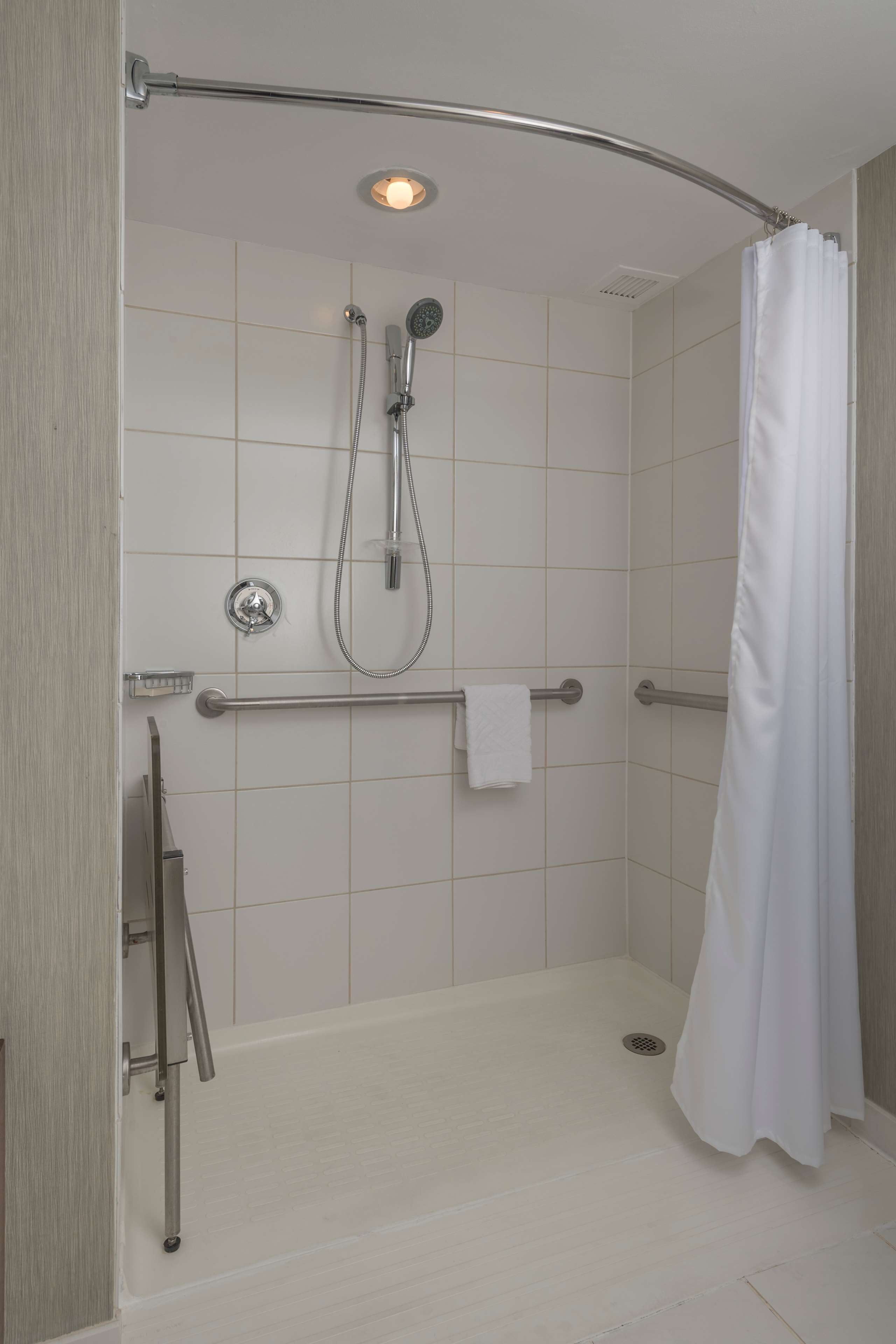 A walk-in shower with a white shower curtain, a handheld showerhead, a wall-mounted faucet, and a grab bar.