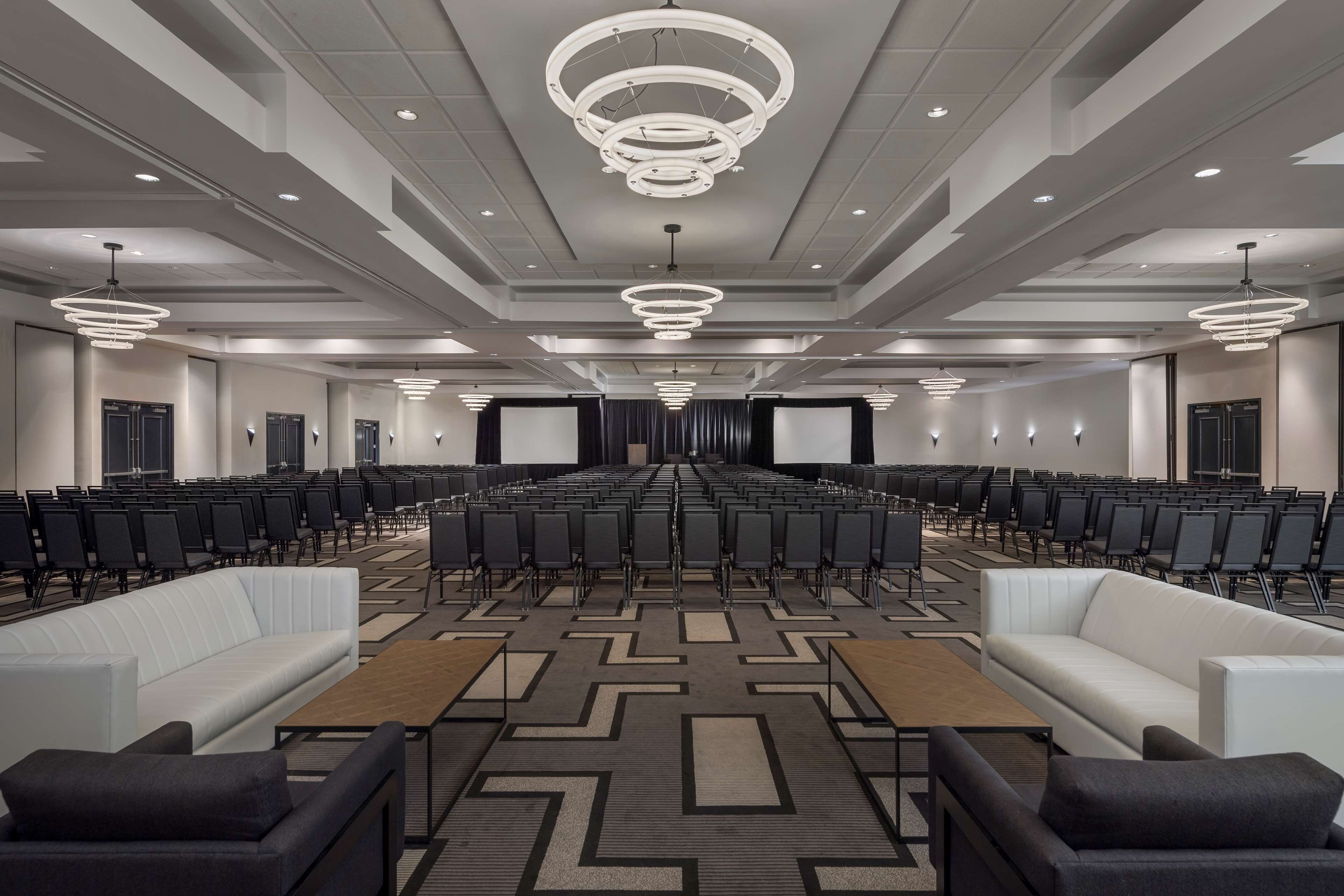 A conference room with rows of chairs, a stage, and a large screen.