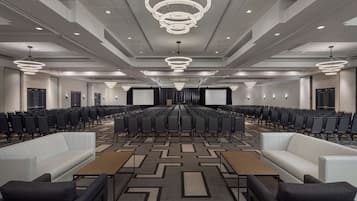 A conference room with rows of chairs, a stage, and a large screen.