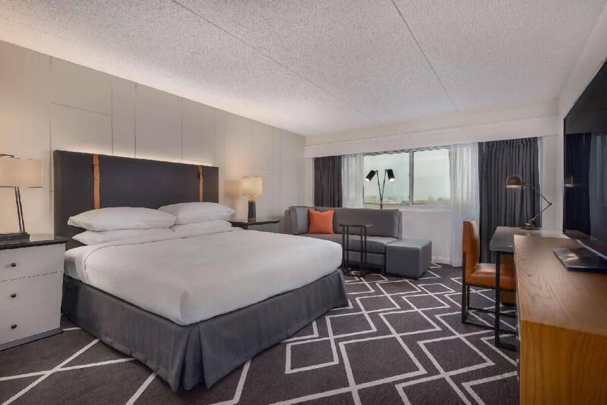 A hotel room with a large bed, a sofa, a desk, and a window with curtains.