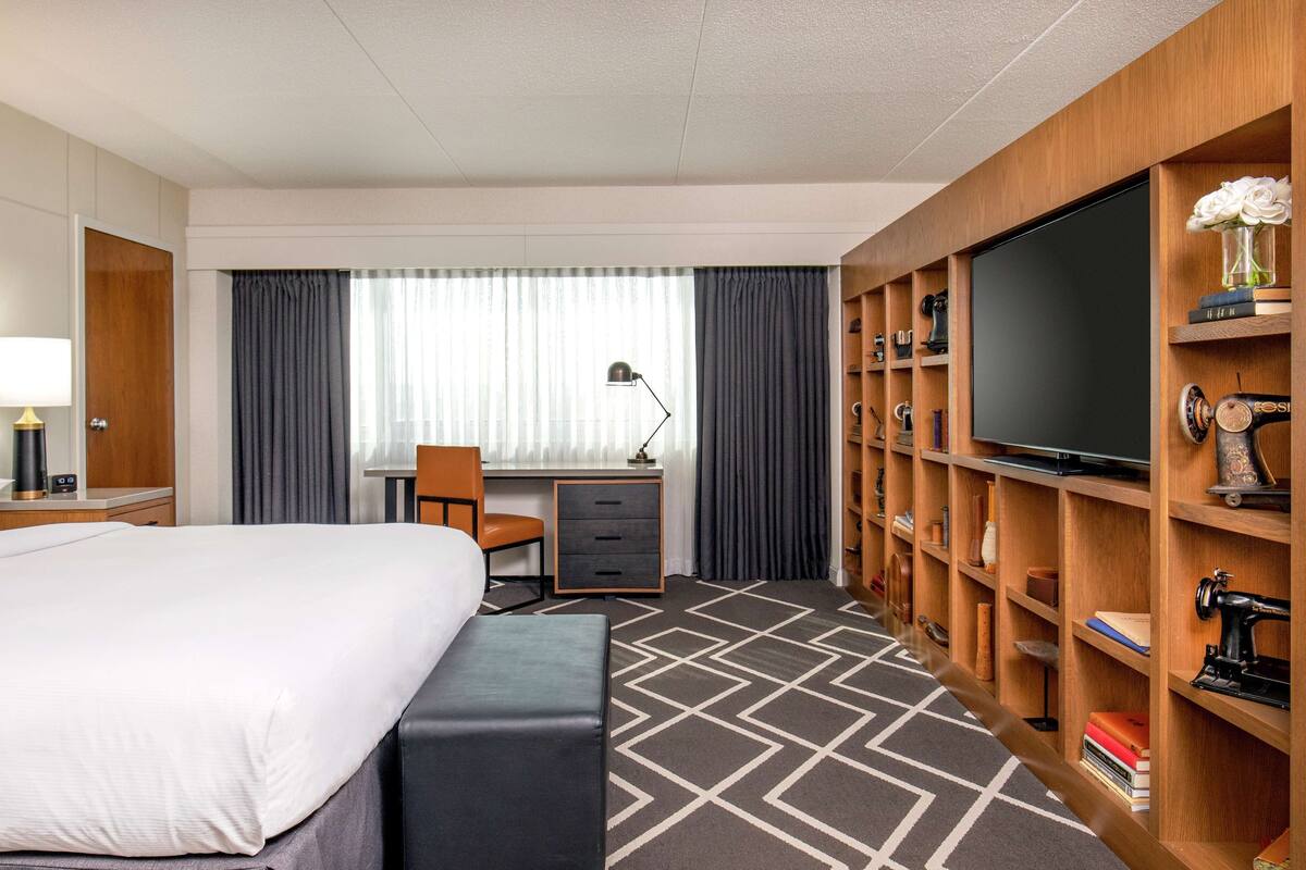 A hotel room with a bed, desk, chair, TV, and a wooden bookshelf.