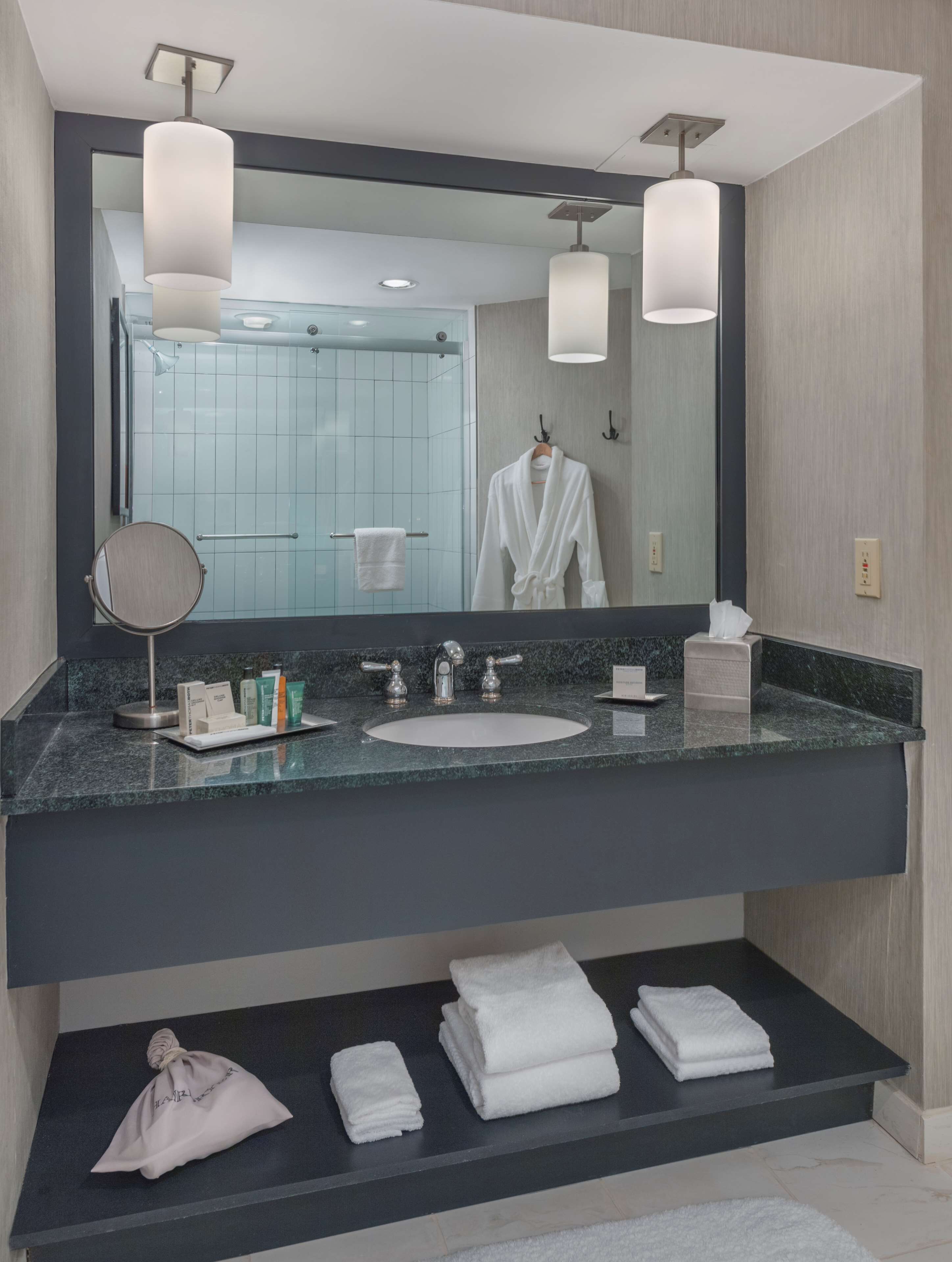A modern bathroom with a large mirror, a sink, and a vanity area. There are towels and toiletries on the counter.