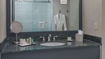 A modern bathroom with a large mirror, a sink, and a vanity area. There are towels and toiletries on the counter.