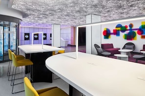 Un interior moderno con un mostrador de recepción curvo, una zona de estar con mesas redondas e instalación artística de colores en la pared.