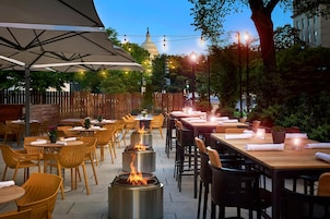 An outdoor dining area with tables and chairs, a pergola with a canopy, and a fire feature.