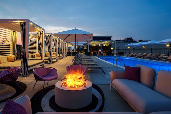 A rooftop pool area with lounge chairs, a fire pit, and umbrellas.