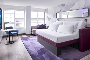 Una habitación de hotel moderna con cama, escritorio, silla y un amplio ventanal.