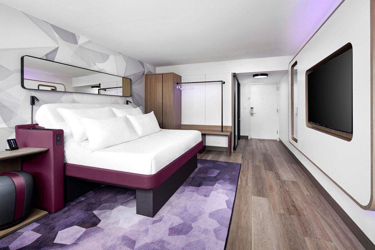 A modern bedroom with a bed, bedside table, TV, wardrobe, and a mirror.