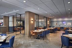 A modern restaurant interior with wooden flooring, tables with blue and brown chairs, and a glass partition wall. - YOTEL Washington DC, Select by Hilton (Washington)