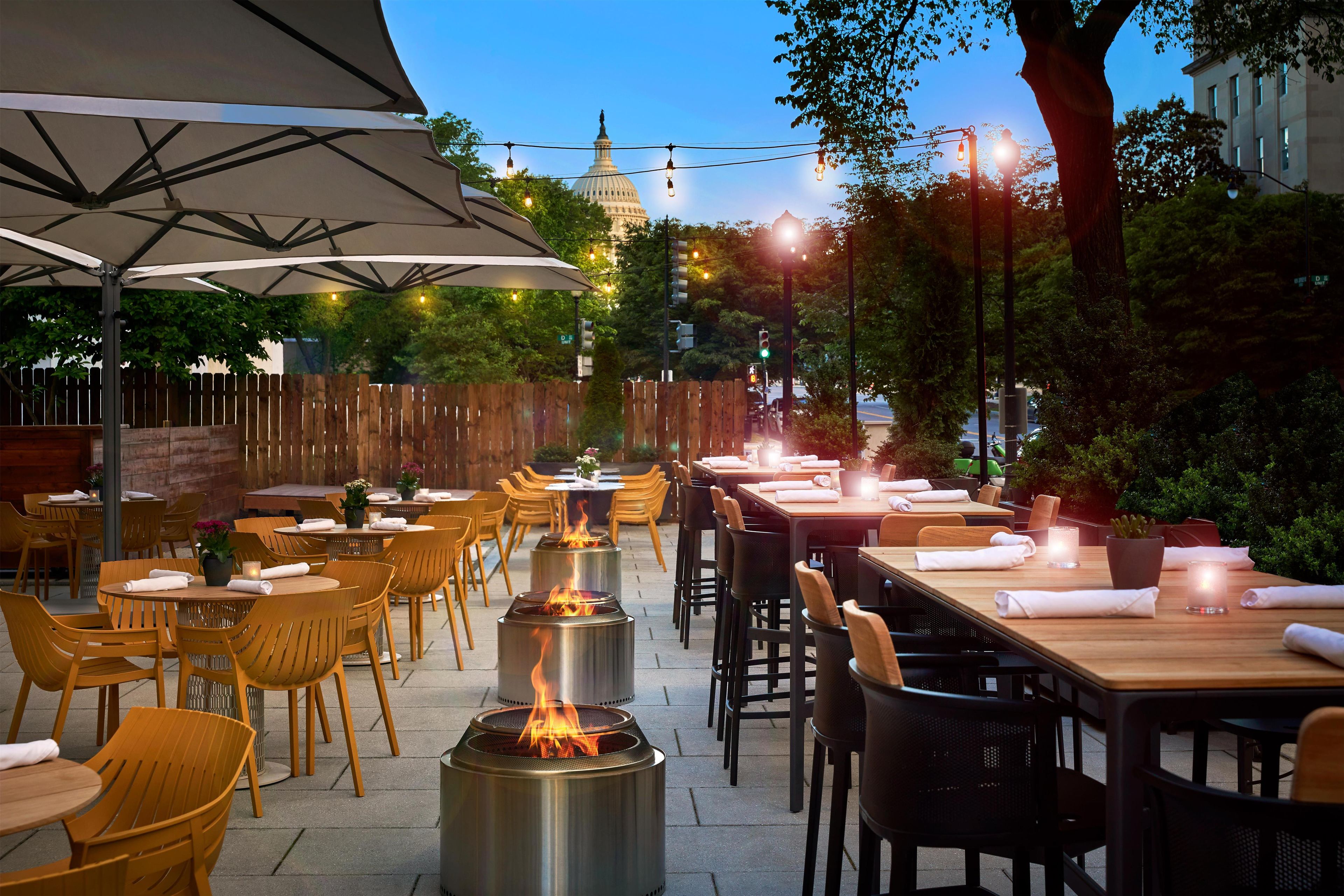An outdoor dining area with tables and chairs, a pergola with a canopy, and a fire feature.
