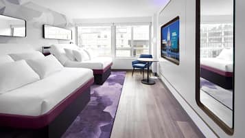 Una habitación de hotel moderna con una cama blanca, una silla azul y un ventanal que ofrece vistas a la ciudad.