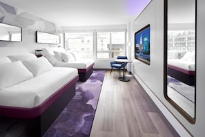 A modern hotel room with a white bed, a blue chair, and a large window offering a city view.
