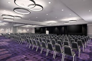 A conference room with rows of chairs, a stage with curtains, and circular ceiling lights. - YOTEL Washington DC, Select by Hilton (Washington)
