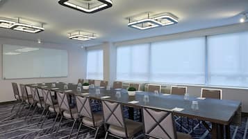 A conference room with a long table, chairs, a whiteboard, and large windows.