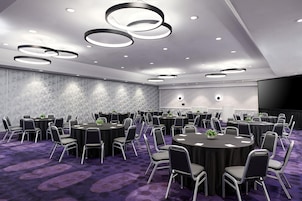 A conference room with multiple round tables, chairs, and a large screen.