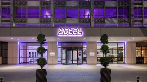 A hotel entrance with a neon sign, glass doors, and potted plants. - YOTEL Washington DC (Washington)