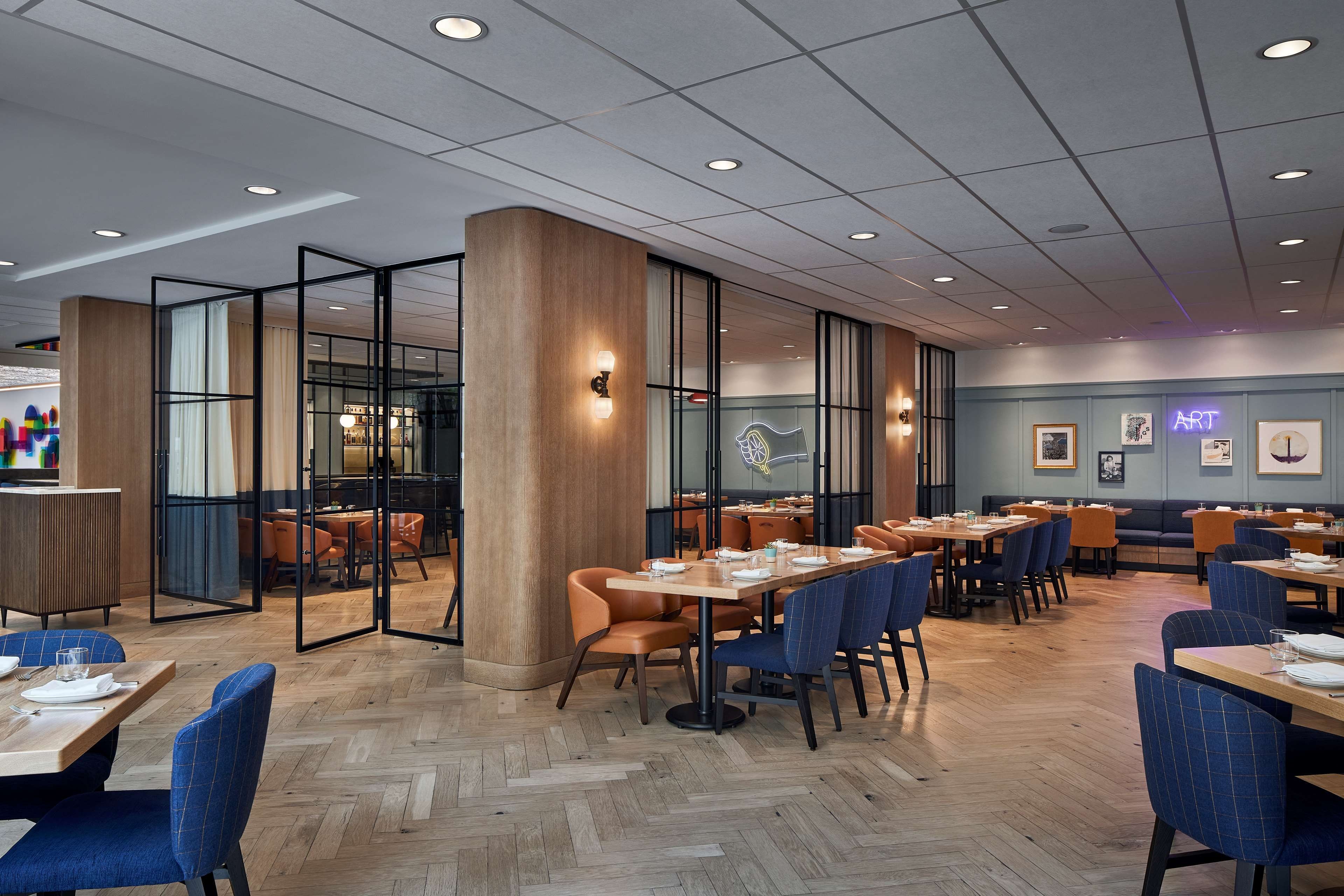 Et moderne restaurantinteriør med trægulv, glasvægge og forskellige sidearrangementer, herunder borde og stole.
