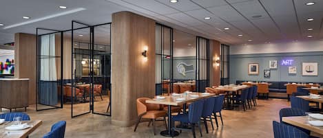 A modern restaurant interior with wooden flooring, glass partitions, and a variety of seating arrangements including tables and chairs.