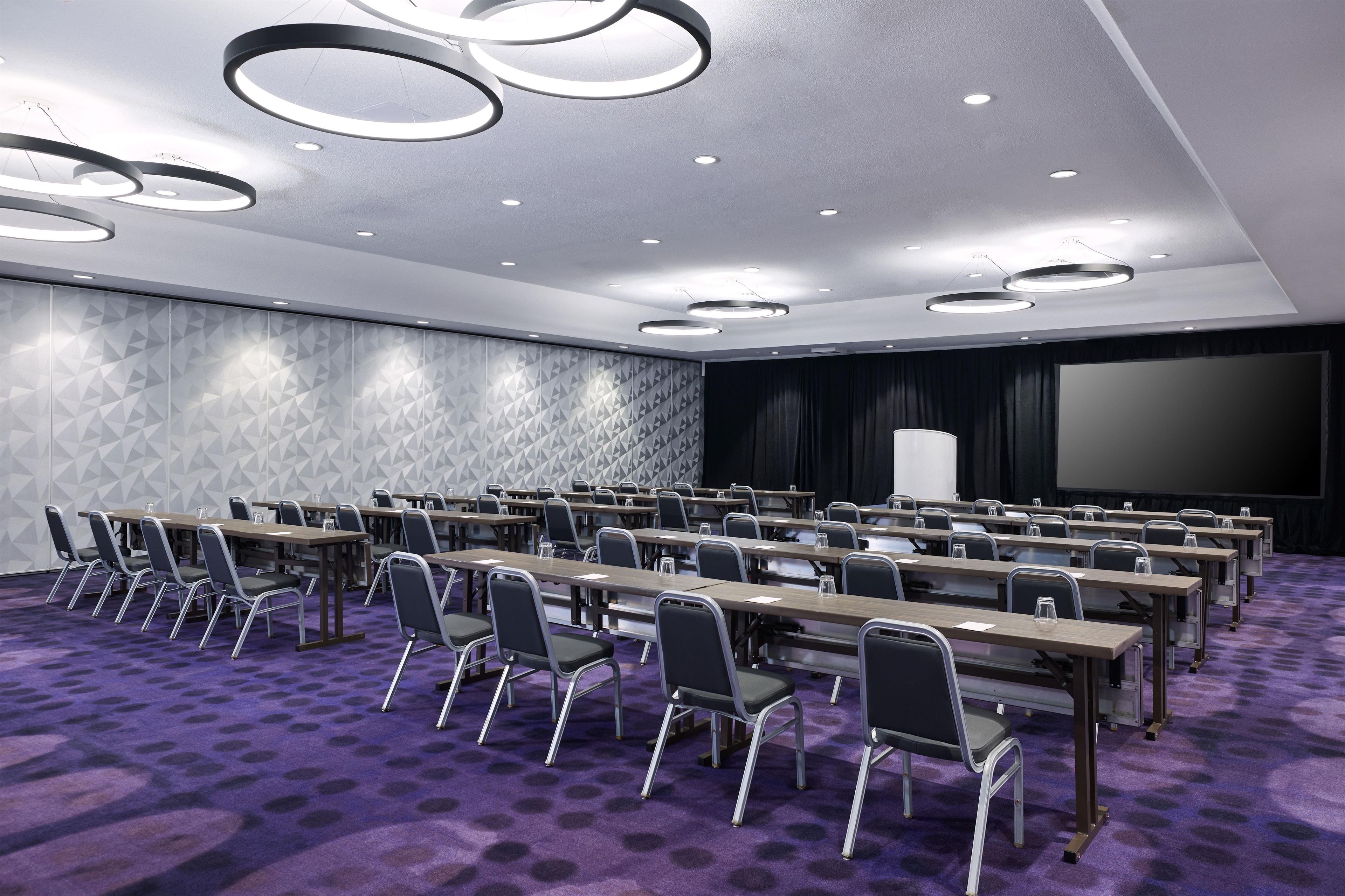 A conference room with a stage, rows of tables, and chairs.