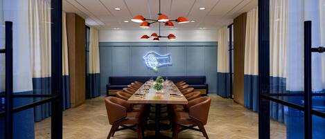 A conference room with a long table, chairs, a neon light, and a ceiling with recessed lighting.