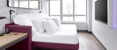 A modern hotel room with a bed, a desk, a chair, a TV, and a window with a city view.