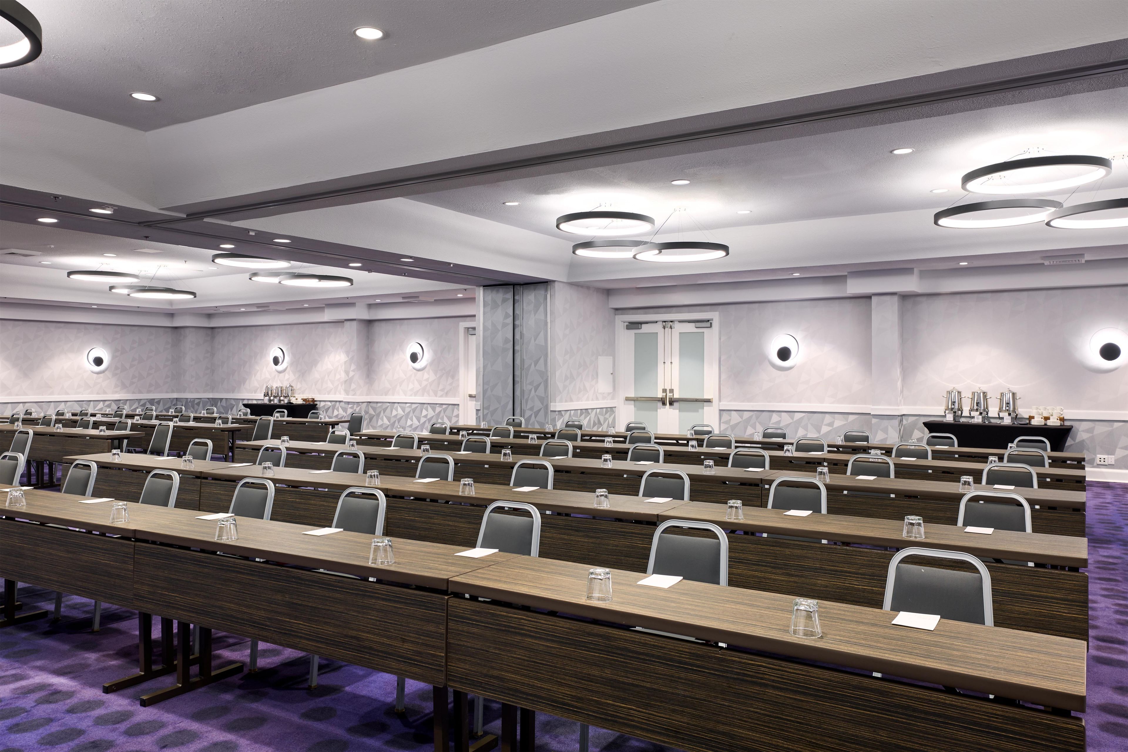 Uma sala de conferência com mesas compridas, cadeiras e um pódio.