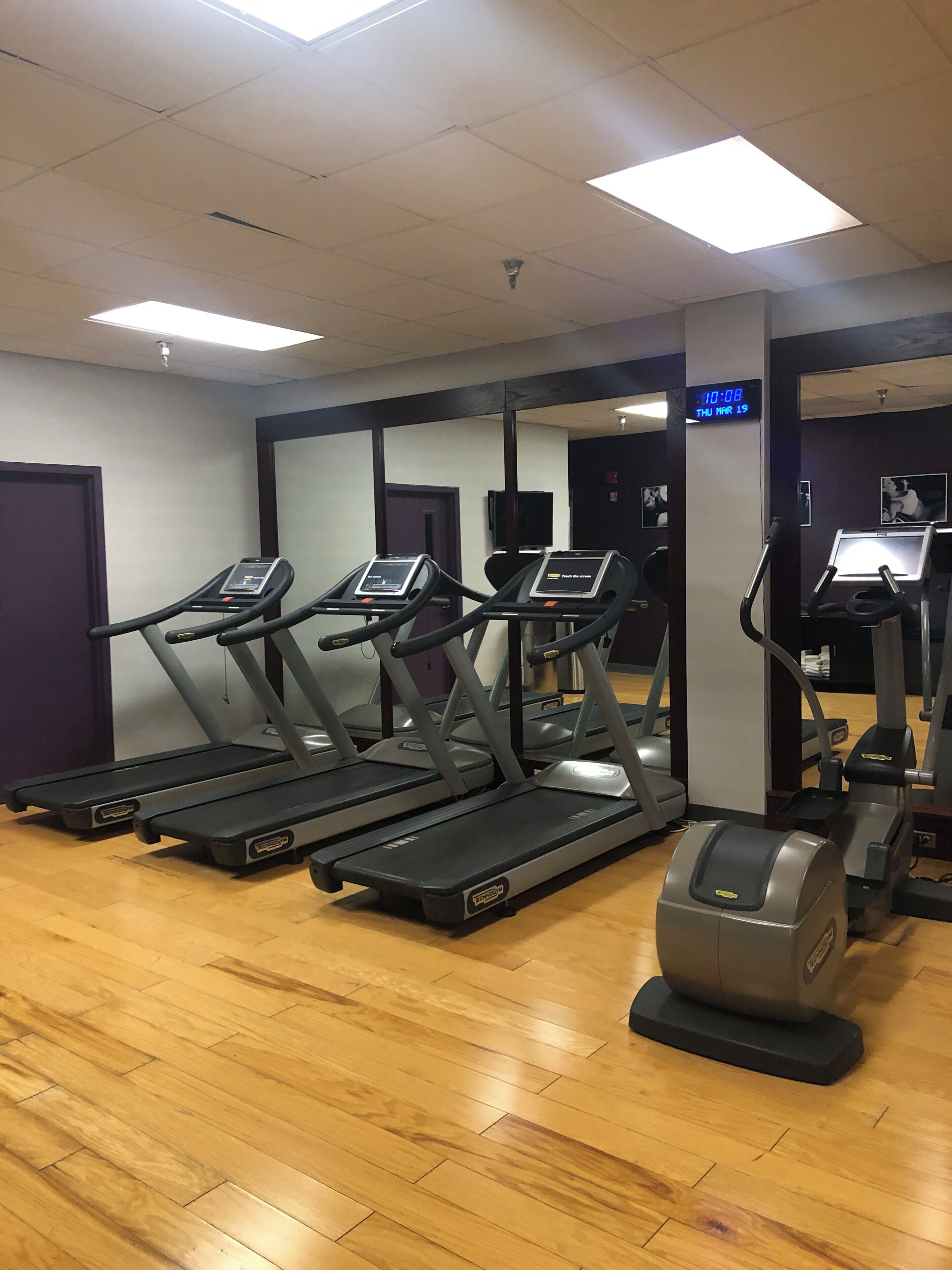 Een sportschool met loopbanden, een hometrainer en een spiegelwand.