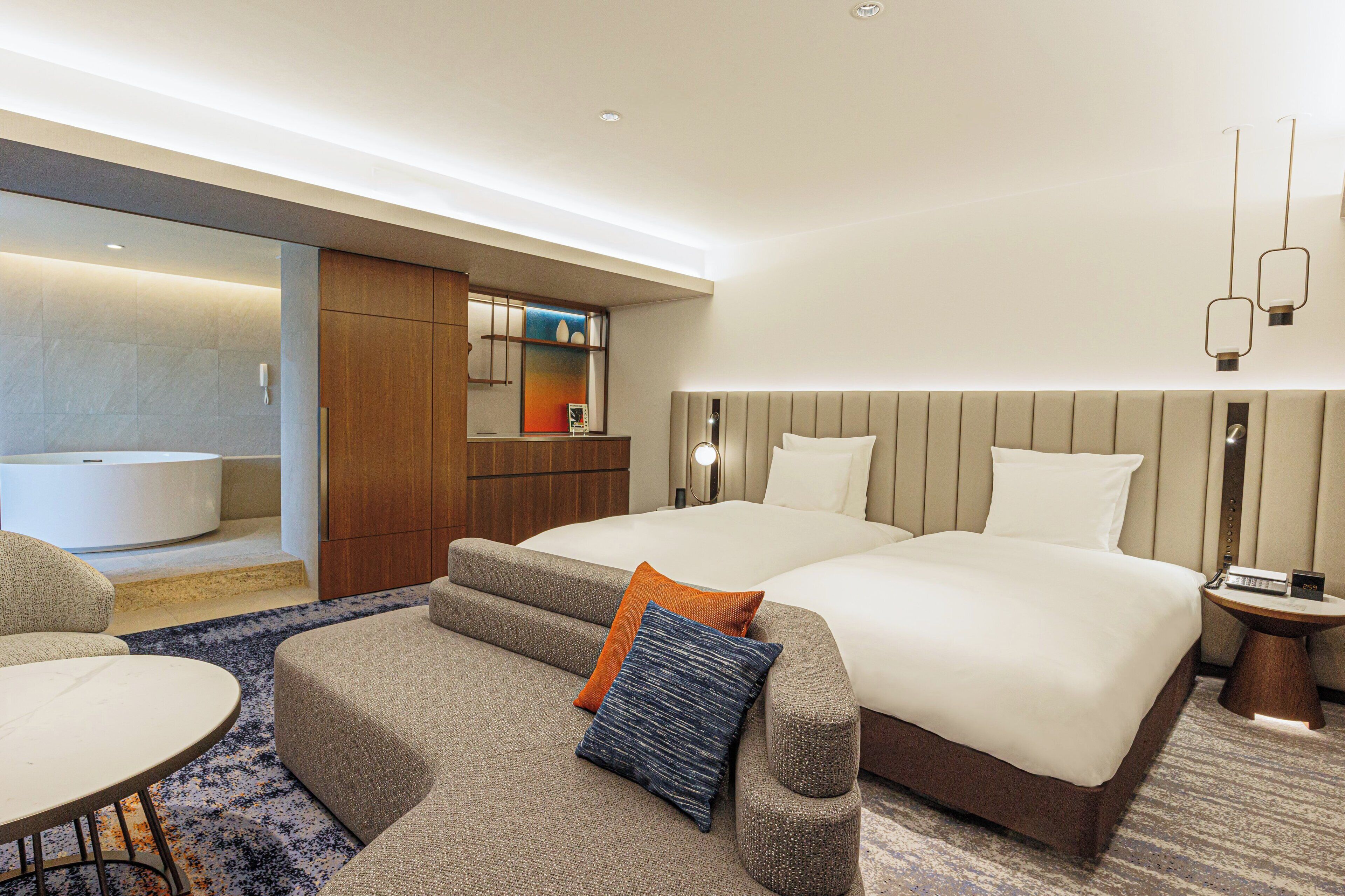 Habitación de hotel con dos camas, un sofá, una mesita, baño y un espejo.