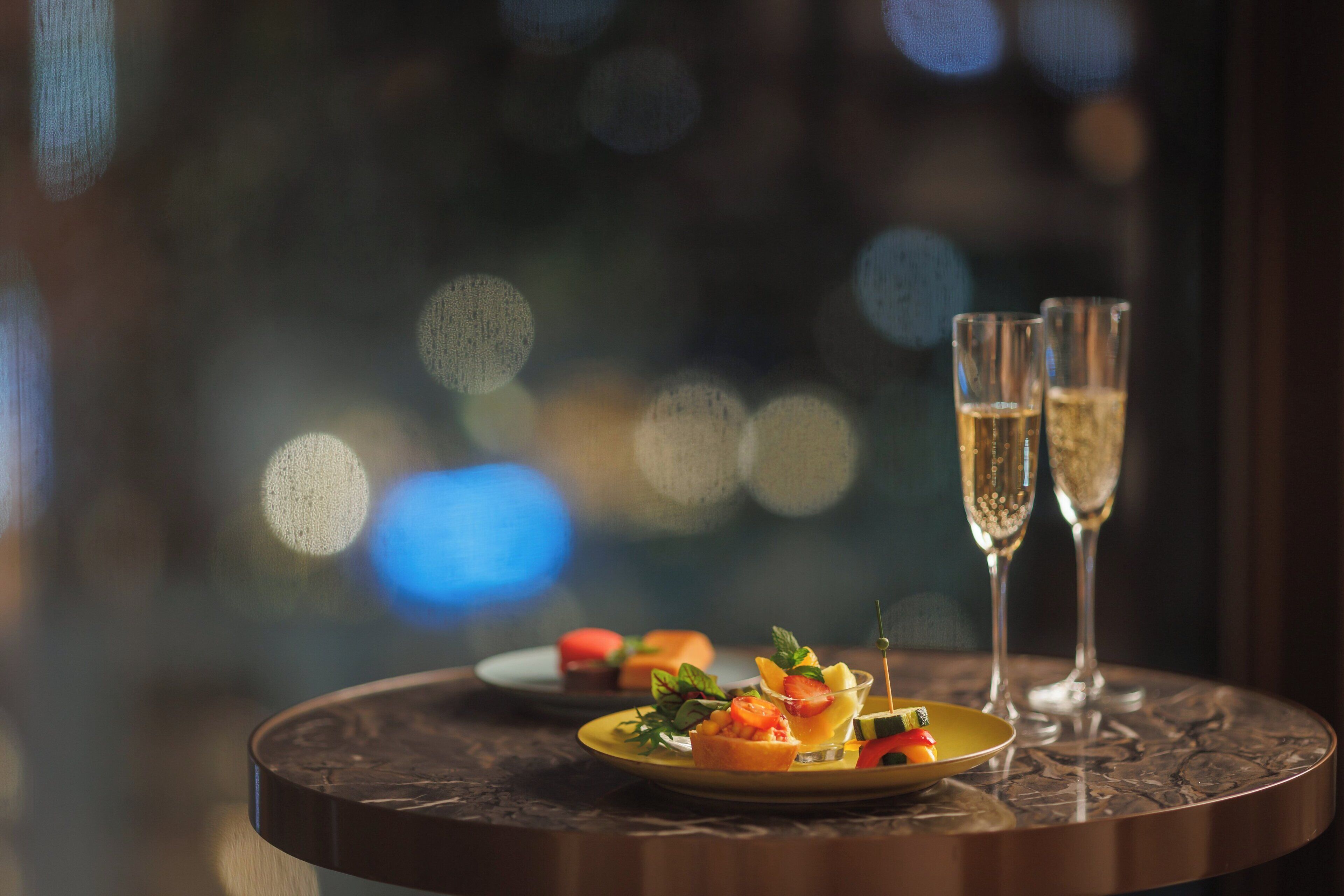 A round table with a plate of appetizers and two glasses of champagne.