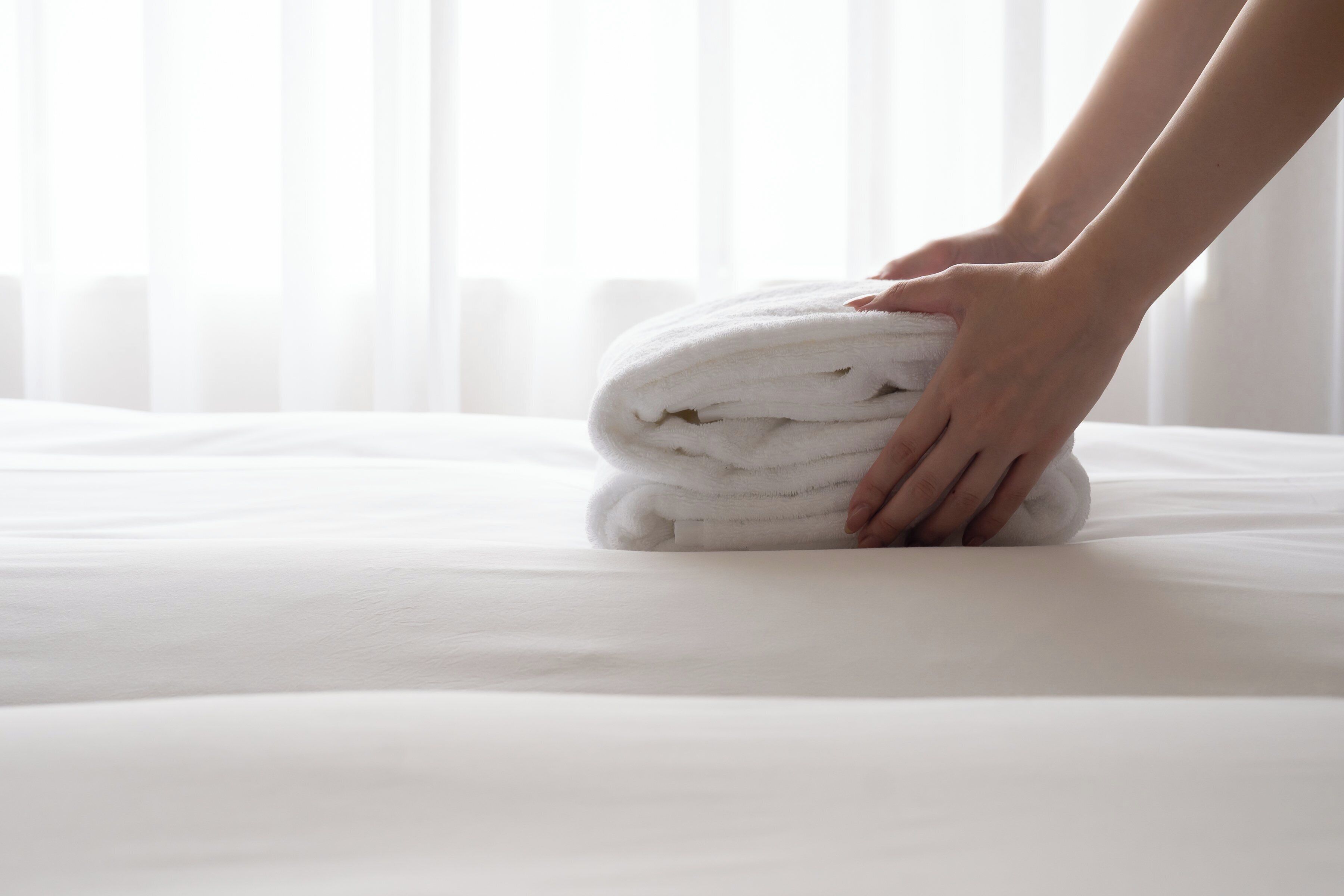 A neatly folded white towel on a bed with a white bedspread.