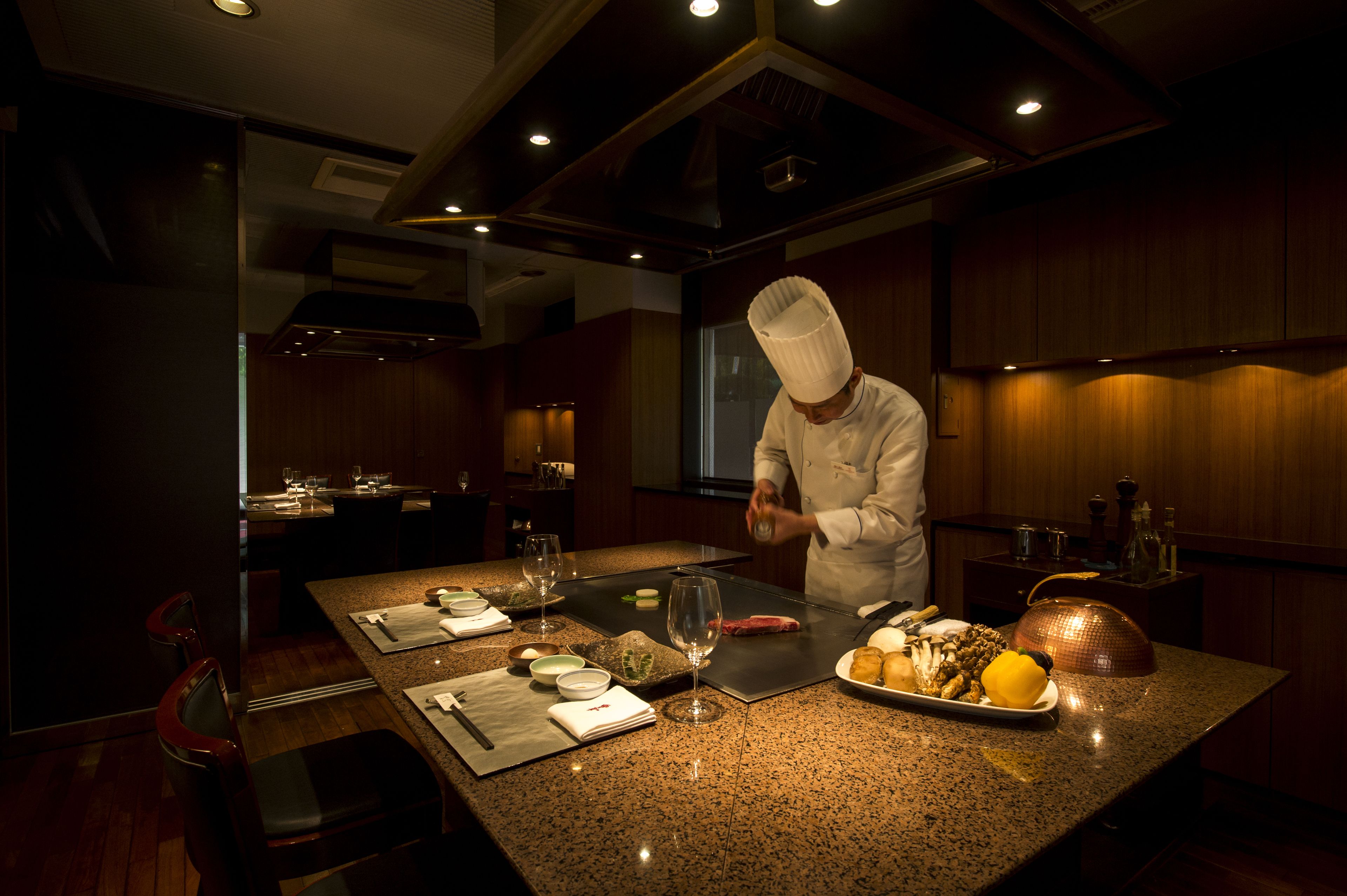 A chef preparing food in a modern kitchen with wooden accents and a polished granite countertop.