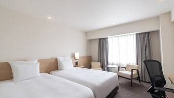 Une chambre d’hôtel avec deux lits, un bureau, une chaise, une petite table et une fenêtre avec des rideaux.