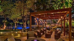 An outdoor lounge area with wicker furniture, a fire pit, and hanging lights.