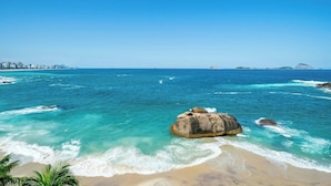 A coastal landscape with clear blue waters, a sandy beach, and a large rock formation.