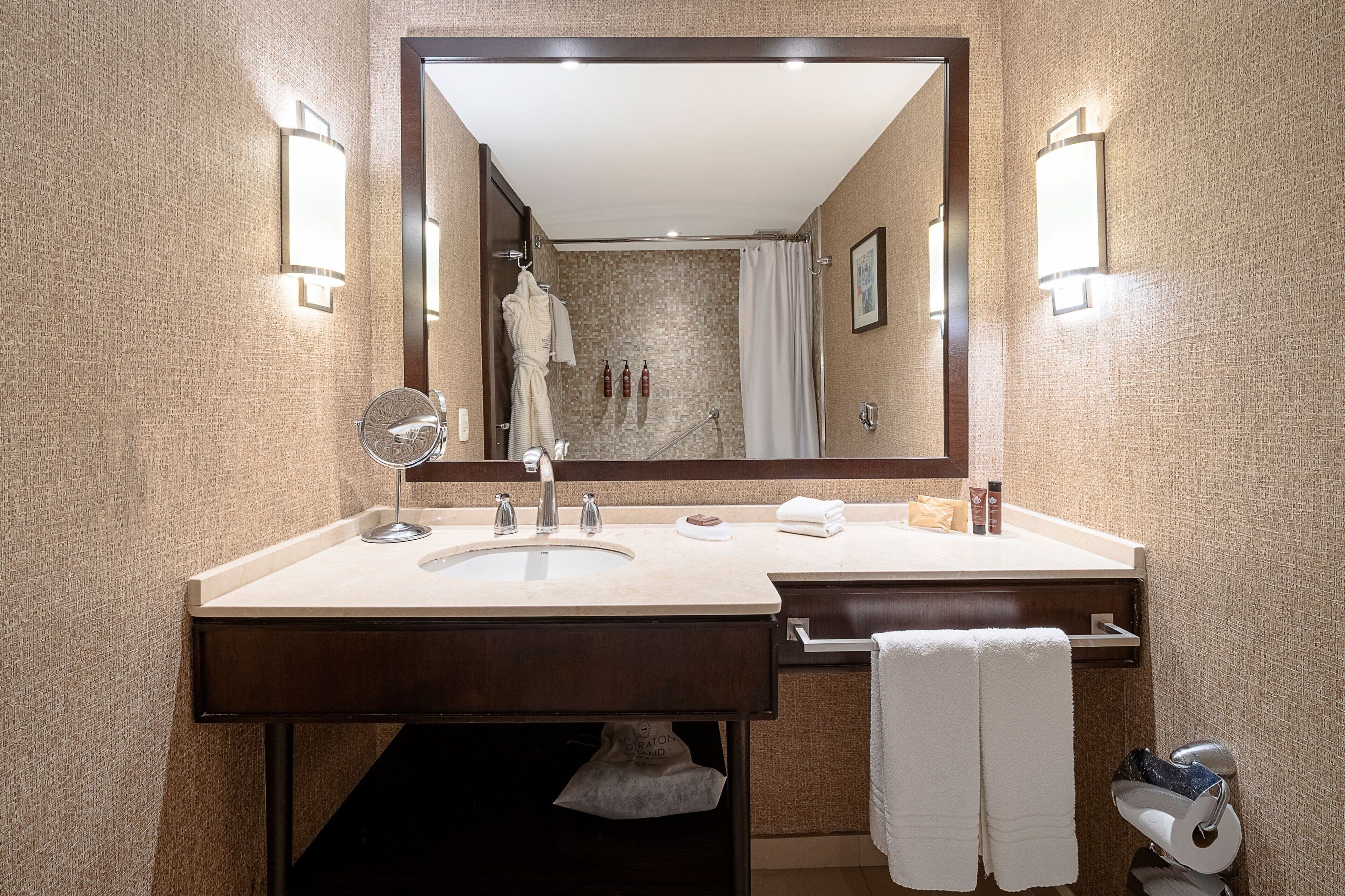 Et moderne badeværelse med et stort spejl, to håndvaske, et håndklædestativ og en bruseniche.