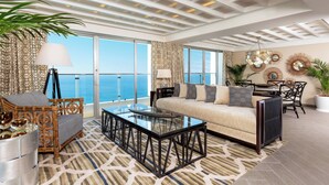 A spacious living area with a sofa, coffee table, and chairs, large windows with a view of the ocean, and decorative wall art.