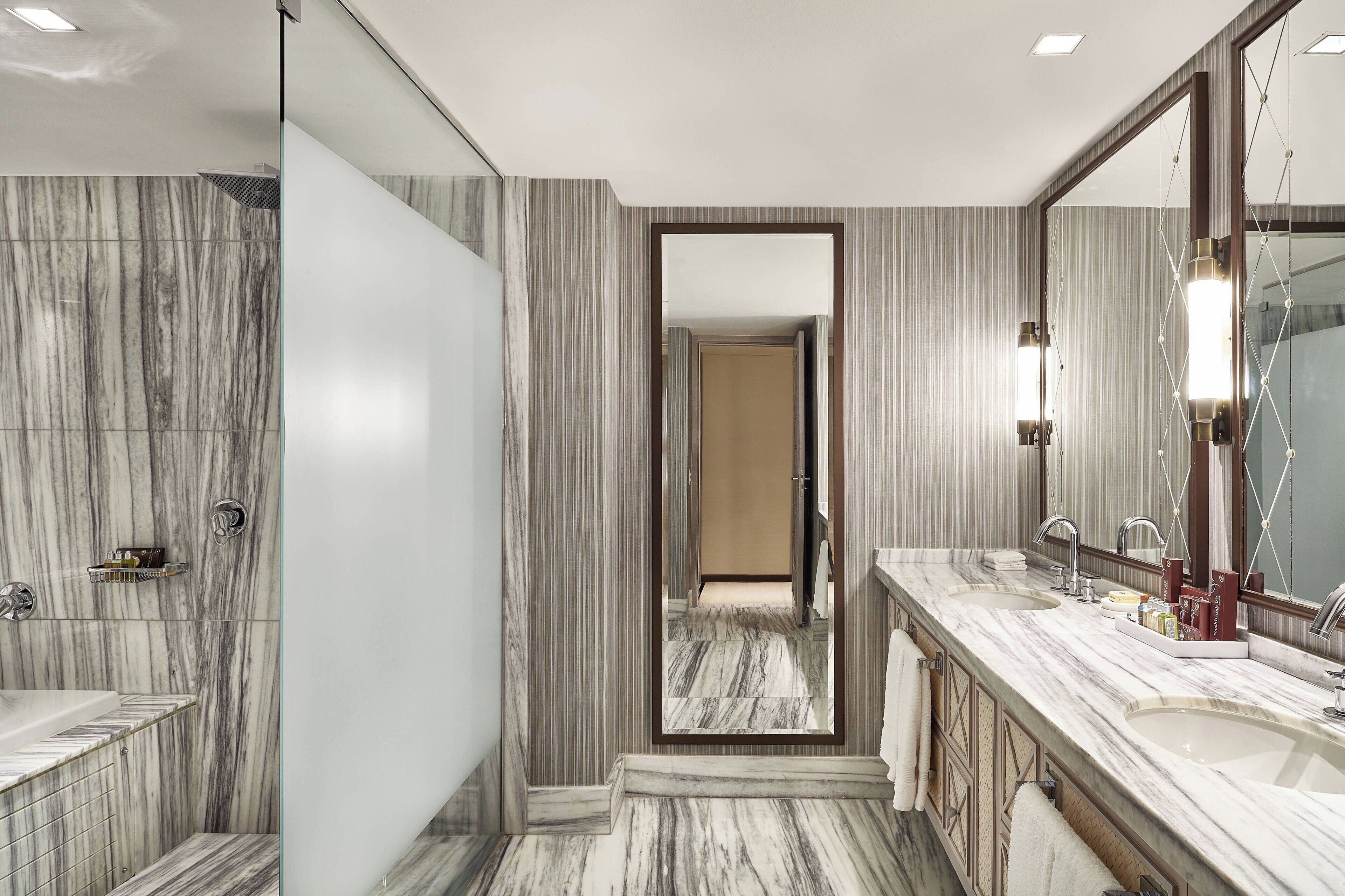 A bathroom with marble walls, a large mirror, and a walk-in shower.