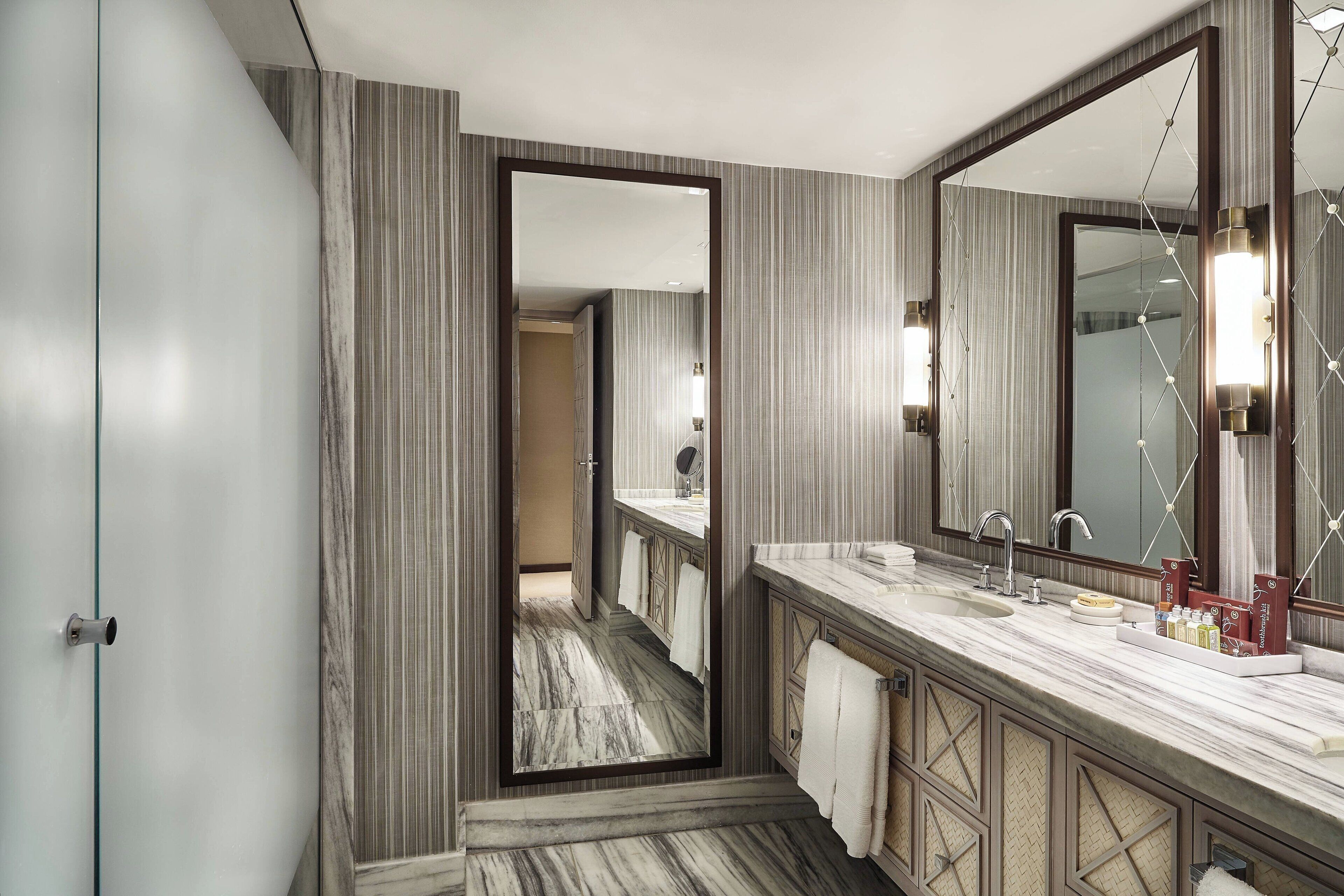 A modern bathroom with a large mirror, marble countertop, and a view into the adjacent room.