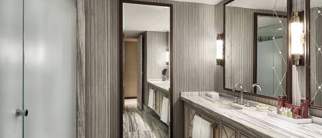 A modern bathroom with a large mirror, marble countertop, and a view into the adjacent room.