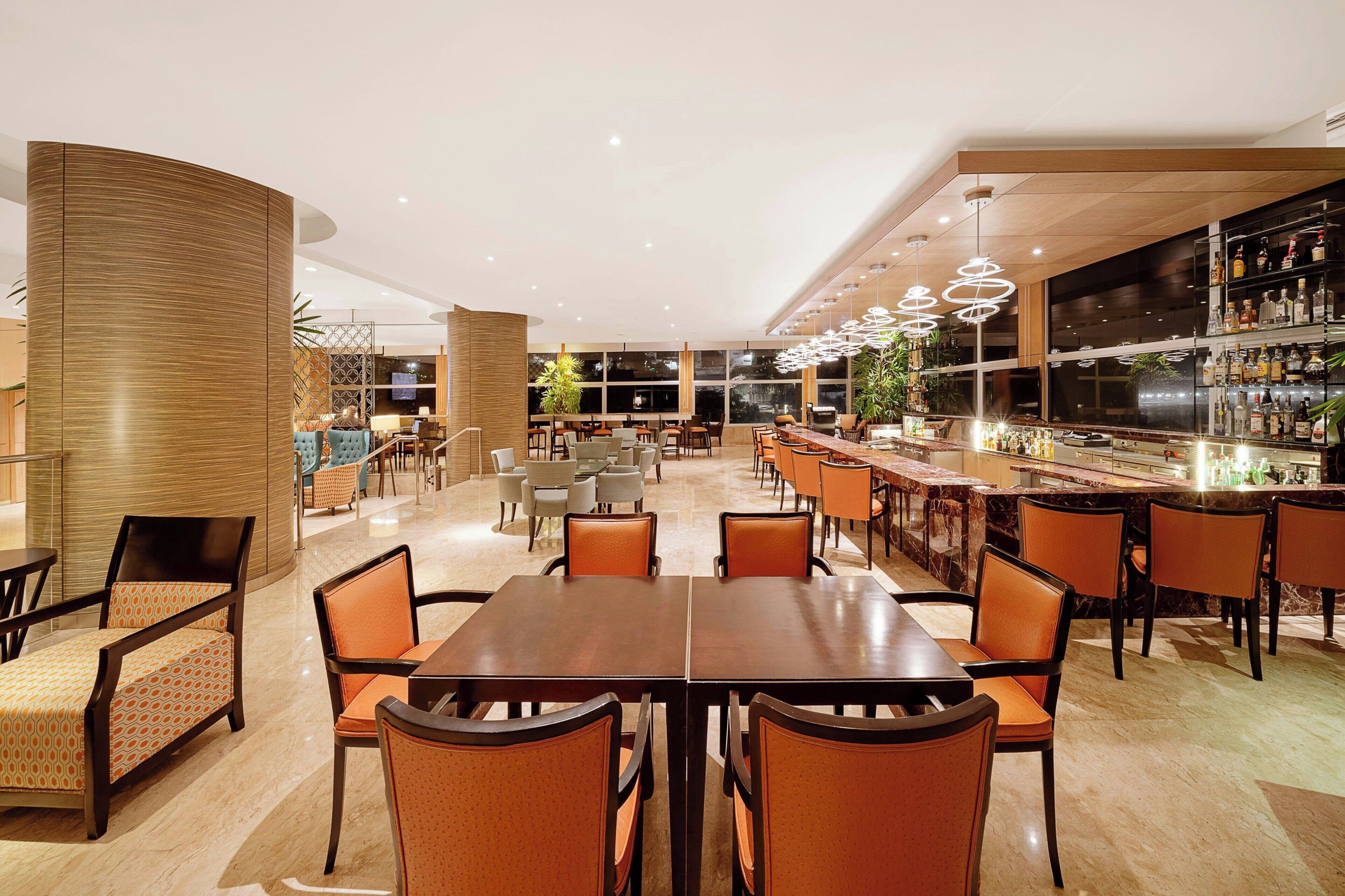 Un amplio vestíbulo de hotel con zona de bar, arreglos de asientos y una recepción.